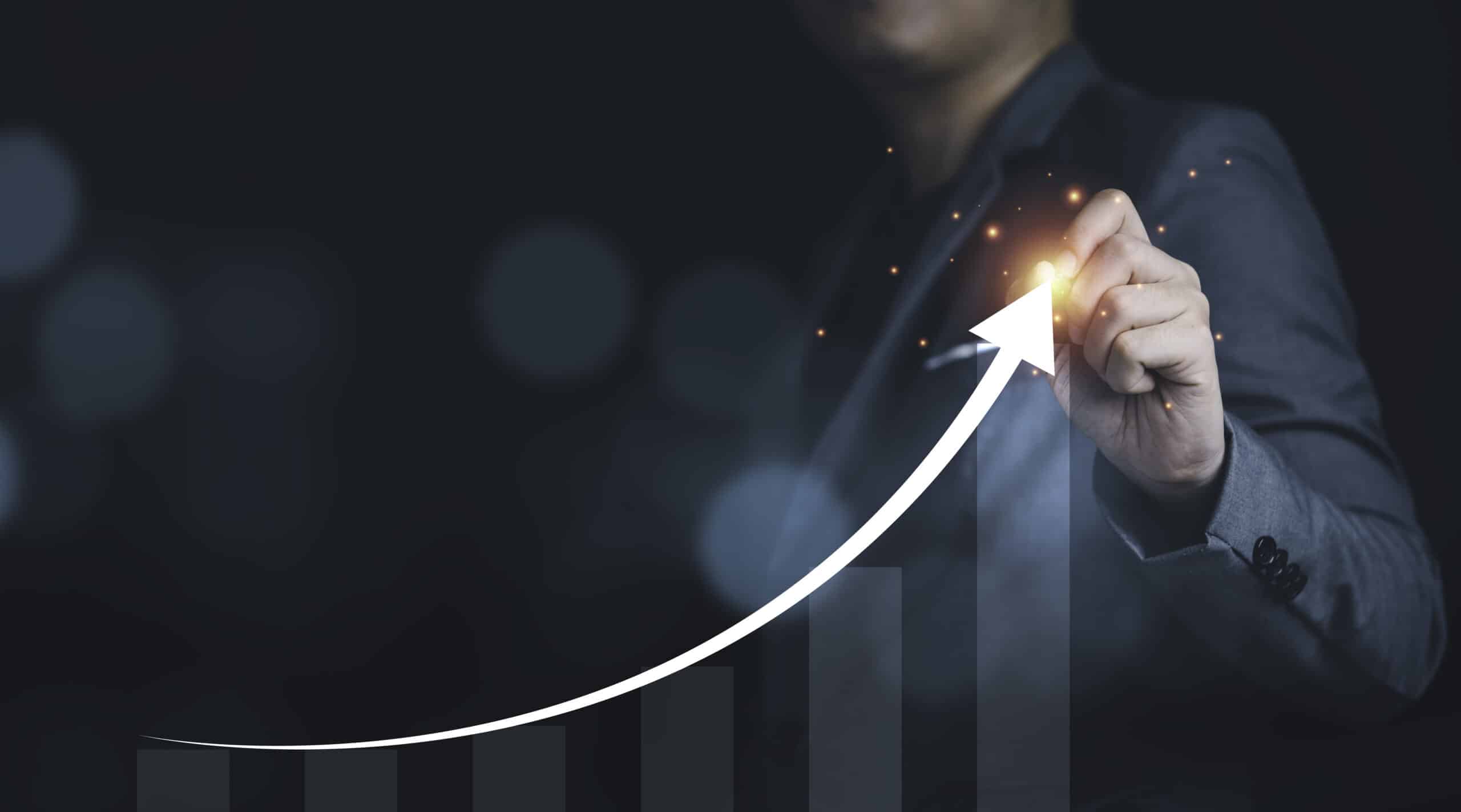 Person in a suit drawing an upward curved arrow on a positive trajectory bar graph